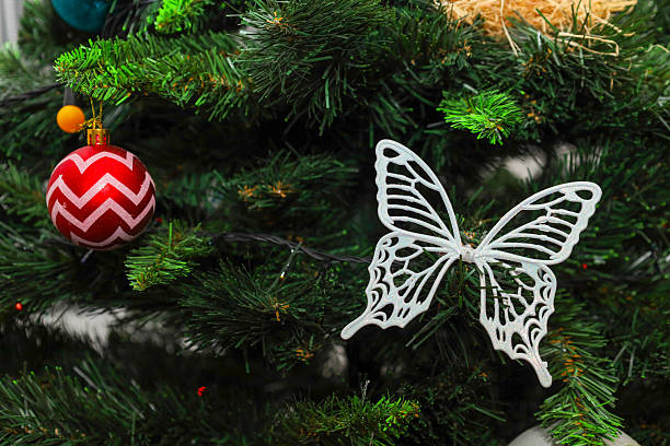 istock An elegant white butterfly figure with openwork wings and a red ball with a zigzag pattern decorate the fluffy branches of a Christmas tree. 2253932682