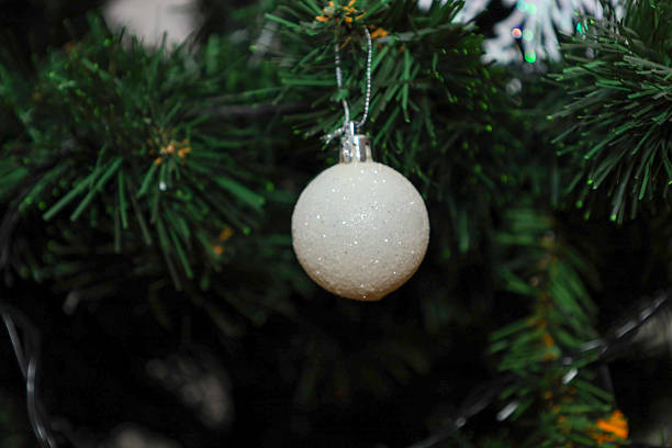 istock A white glittery ball ornament hangs on green Christmas tree branches, creating a festive atmosphere of comfort. This elegant holiday bauble sparkles against pine needles, adding charm to winter decor and highlighting the joy of celebrations. 2253932724