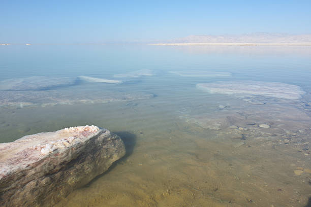 Beautiful landscape of the Dead Sea coastline with a big stone covered the crystal of salt in summer morning