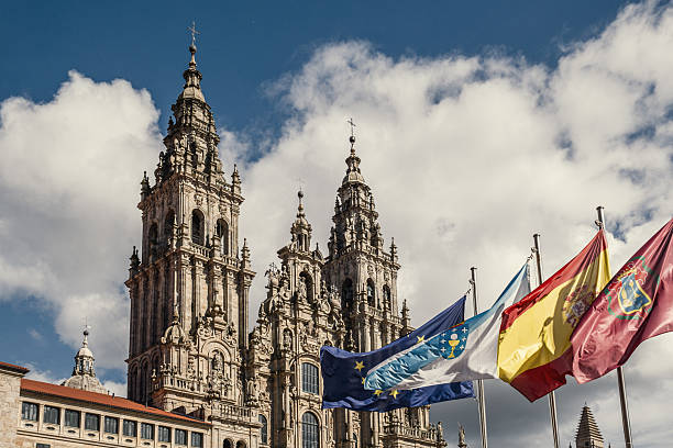 The Cathedral of Santiago de Compostela with its imposing Baroque architecture and bell towers, with four flags flying in the foreground representing, from right to left: the city of Santiago de Compostela, Spain, Galicia and being part of Europe.