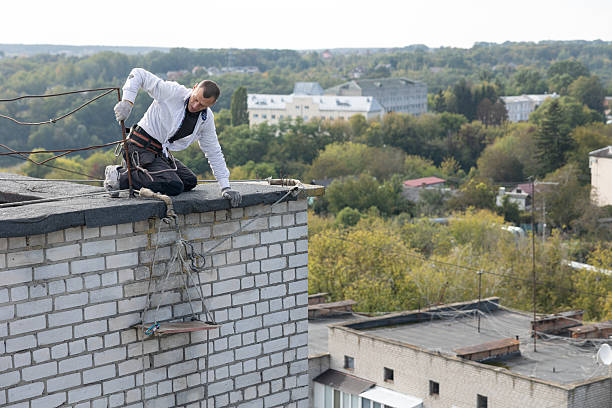 Construction worker works on the edge of the roof of a multi-story residential building. He lowers a safety harness seat system with the seat for working at height. The worker is preparing to insulate the building facade on the ninth floor using polystyrene panels.