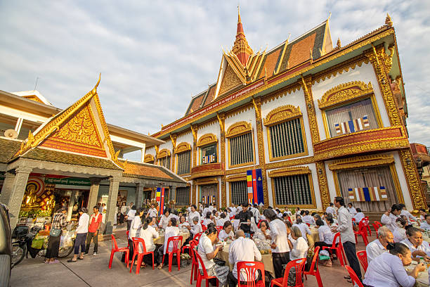 White statue with hands together in prayer position, with a buddhist temple in the background, in phnom penh, cambodia