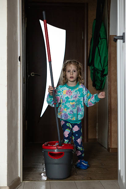 A fashionable young woman with mop and bucket standing against a yellow background, showcasing a playful and trendy lifestyle.