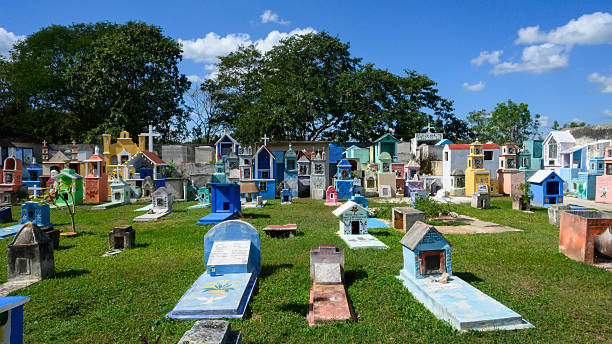 Hoctun, Yucatan, Mexico - 26th of December, Painted tombs and religious memorials lining a quiet cemetery passage under bright daylight