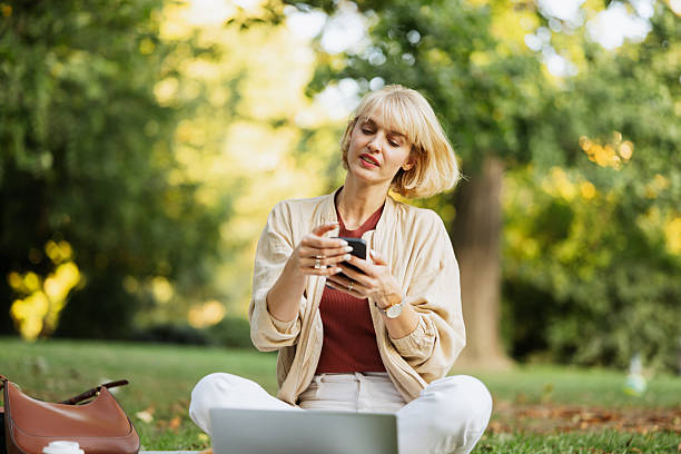istock Woman using smartphone while sitting on grass in park during daytime 2253936568