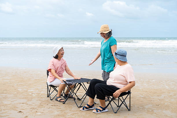 istock Senior women enjoying and talking while sitting on folding chairs on tropical beach. Asian female relaxing on summer vacation after retirement. 2253936835