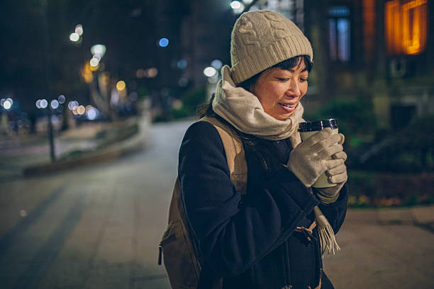 A smiling woman walks through the city at night holding a takeaway coffee, enjoying a calm urban evening.