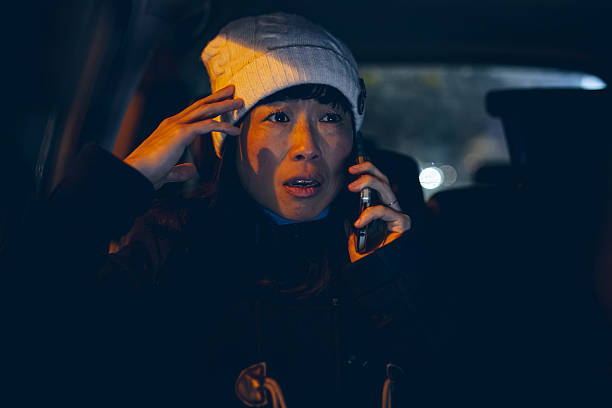 A woman looks concerned while talking on her phone and sitting in a car during a delayed nighttime commute