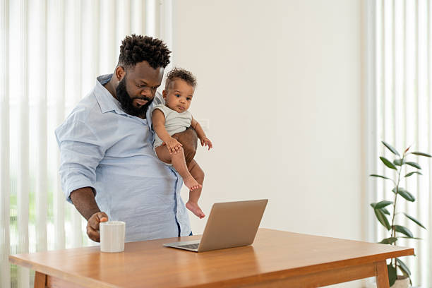 istock African father multitasking holding baby son, using laptop and drink coffee while work from home. Single dad parenting newborn boy at modern apartment 2253938373