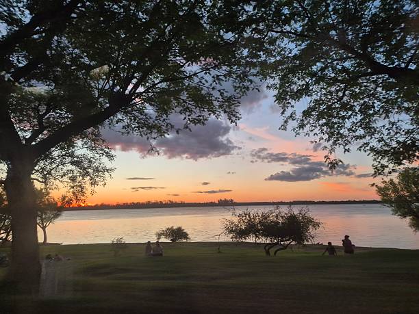 istock Golden sunset over calm river with people relaxing on shore 2253940194