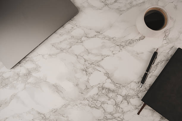 istock A clean workspace is shown with a laptop, black notebook, silver pen, and coffee cup set on a marble tabletop, offering ample copy space for text or notes 2253949364