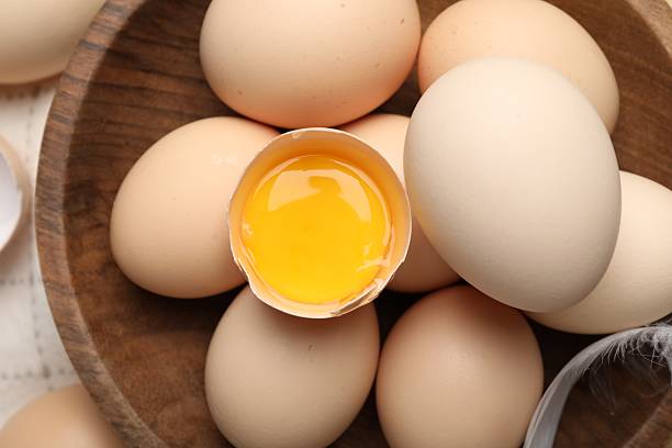 istock Raw chicken eggs in bowl and feather on table, top view 2253952371