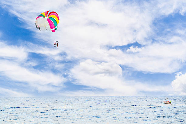 Two people parasailing under a colorful parachute in the sky