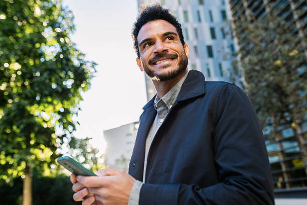 istock Smiling man looking away while holding smartphone in city center 2253954209
