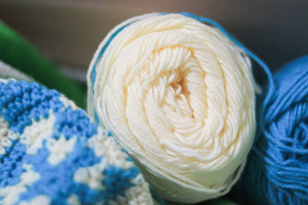 A close up view of a soft cream colored yarn roll alongside blue and white crochet fabric displaying the intricate fibers and textures of the craft materials