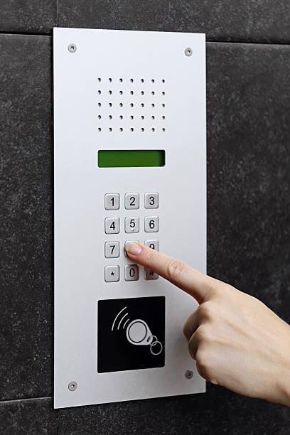 Intercom keypad with a hand pressing a button Close-up of a hand pressing a button on a modern intercom keypad mounted on a dark textured wall. liftmaster entry systems stock pictures, royalty-free photos & images