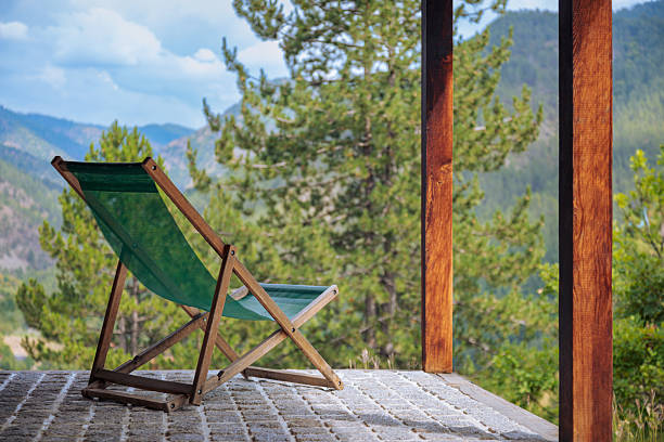 Deck chair on a stone patio overlooking a vast forest and mountain landscape on a sunny day.