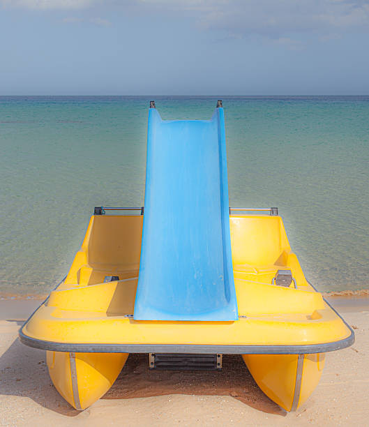 Yellow pedal boat with slide on a calm beach. A playful and serene coastal scene ideal for editorial use.