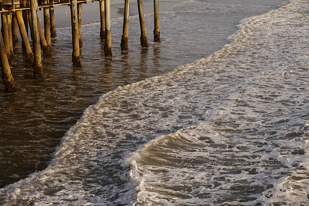 Rusty and weathered pillars of a pier. Waves break between the pillars. Rough North Sea, crashing waves, churning sea. Sunny day, beach at The Hague, Netherlands.