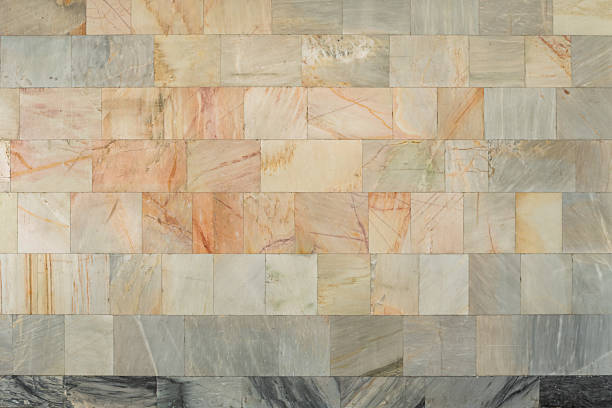 Wall faced with rectangular marble tiles in pastel tones with black marble on the bottom.