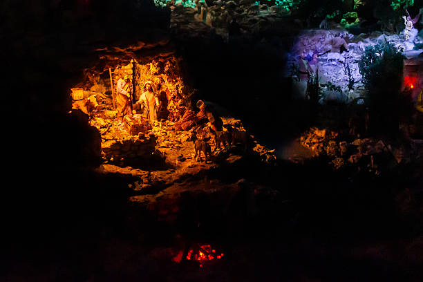A tranquil nativity scene carved into a rocky cave, illuminated by orange and blue lights. Figures, animals, and rustic stone walls create a timeless Christmas tableau with a peaceful, reverent mood.