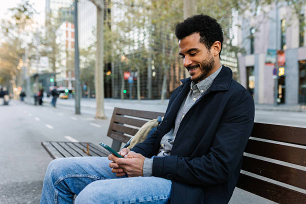 istock Young man checking smartphone while sitting on park bench in city 2253962367