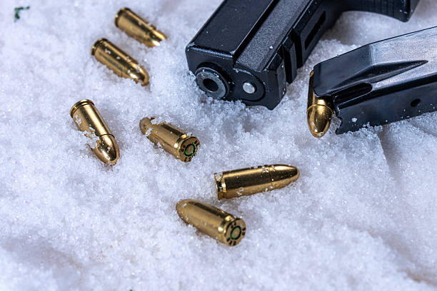 istock Black pistol muzzle and scattered unspent 9mm cartridges on snow 2253964674