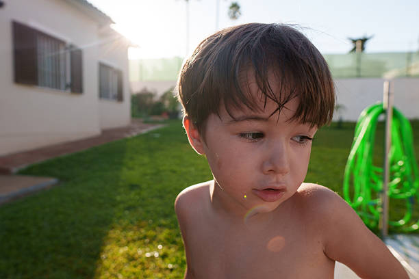 Young child with wet hair standing in backyard during sunny summer day