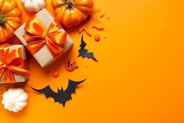 istock Top view of bright Halloween gift boxes and pumpkin decorations festively arranged on a orange surface. Happy Halloween holiday concept 2253970081