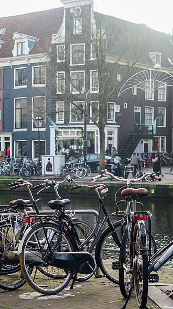 Editorial image taken on December 22, 2025, showing bicycles parked along Prinsengracht canal in Amsterdam, Netherlands. The scene features traditional Dutch canal houses with steep gabled roofs and large windows, a leafless tree, and a classic streetlamp. Boats are moored in the canal, and pedestrians are visible near the buildings