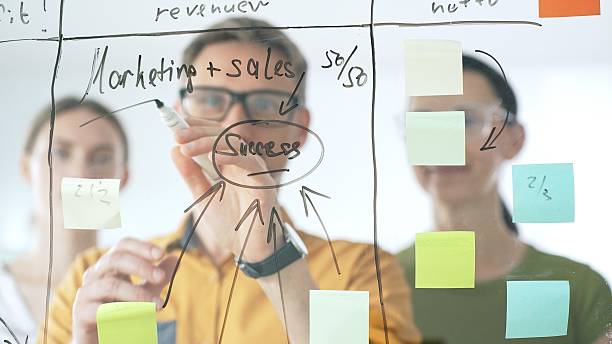 istock Marketing team collaborating, strategizing business growth with colorful sticky notes on transparent board, targeting revenue and profitability goals 2253972576