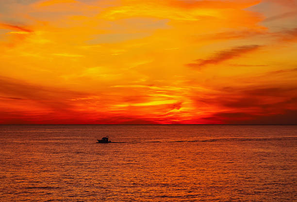 Scenic autumn seascape featuring a single boat at sunset. Tranquil outdoor scene and minimal background.