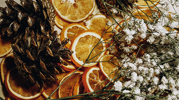 Image taken during a Christmas wreath-making workshop. The composition features glossy pinecones, thinly sliced dried oranges, and delicate sprigs of baby’s breath (Gypsophila), arranged on a natural surface. The warm tones of citrus and earthy textures of cones are softened by the airy white blossoms, creating a festive and rustic visual. The image evokes seasonal craft traditions and the tactile joy of handmade holiday decor