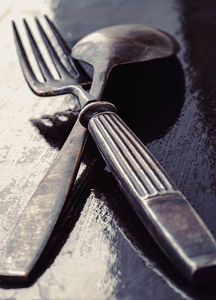 Ancient worn vintage cutlery on the dark background. Crossed black metal spoon and fork in dark tone, Highlighting its texture and design, use it as your Space for text, Design, Wallpaper and Poster, Selective focus.
