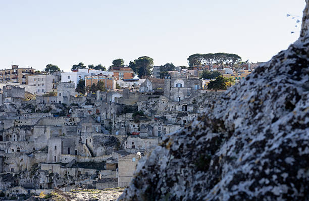 ancient sassi di matera cave dwellings carved into limestone hills under a clear blue sky, historic southern italian architecture and urban heritage