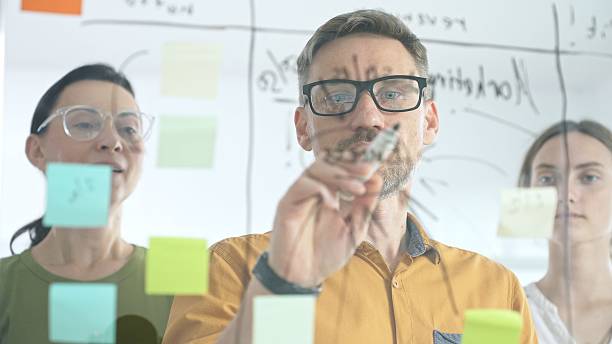 istock Professional team brainstorming project strategy, placing colorful sticky notes on glass board, analyzing data, sharing insights, developing collaborative solutions 2253983309