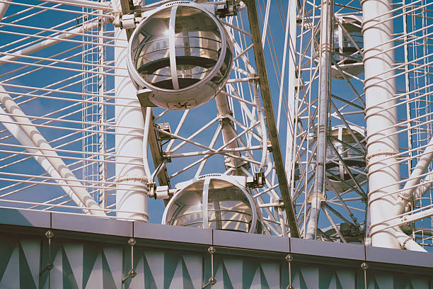 Low angle view of modern white Ferris wheel passenger cars against a vibrant clear blue sky. The image features a vertical minimalist composition with copy space, creating a relaxing summer holiday atmosphere.