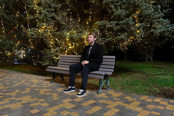istock A person sits quietly on a bench in a park surrounded by trees lit at night 2253988897