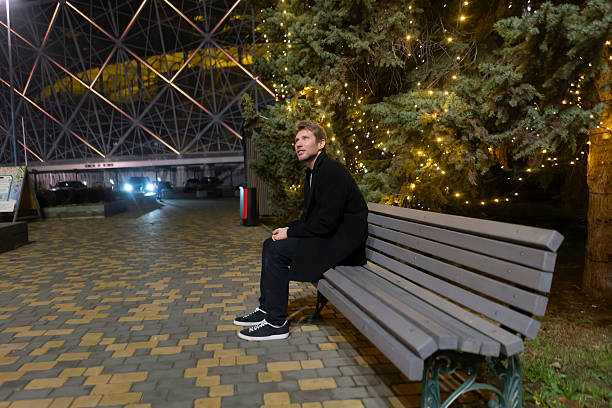 istock A man sits on a bench looking around in a park filled with lights at night 2253988901