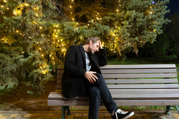 istock A man sits on a bench in a park at night, illuminated by lights from surrounding trees 2253988905