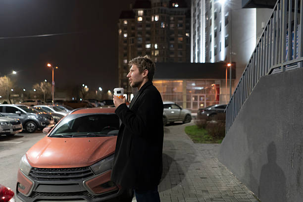 A man is outside in a parking area holding a cup while looking away at night.
