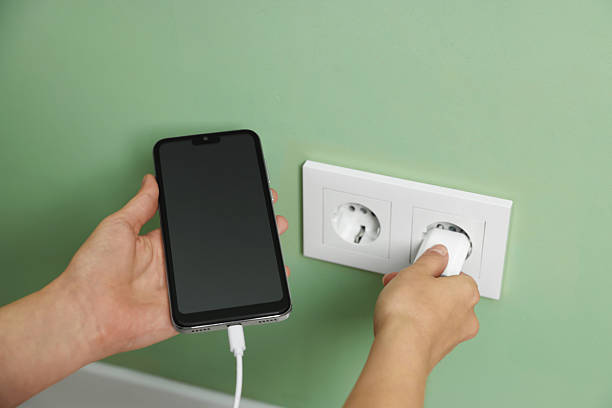 istock Woman plugging smartphone into power socket indoors, closeup 2253993471