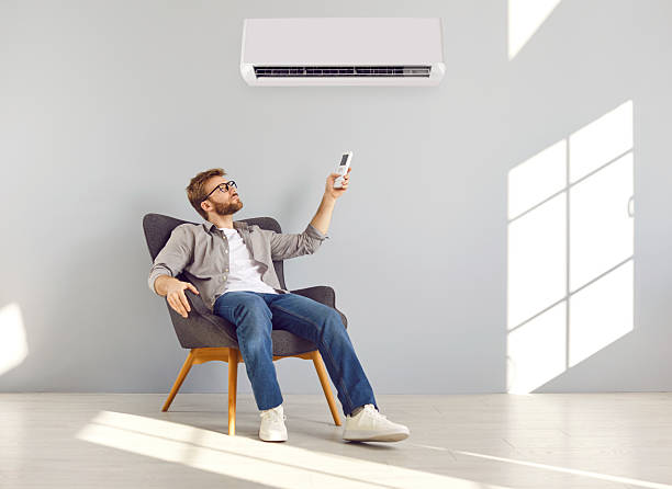 istock Relaxed young man sitting in armchair and setting temperature on air conditioner 2253997797