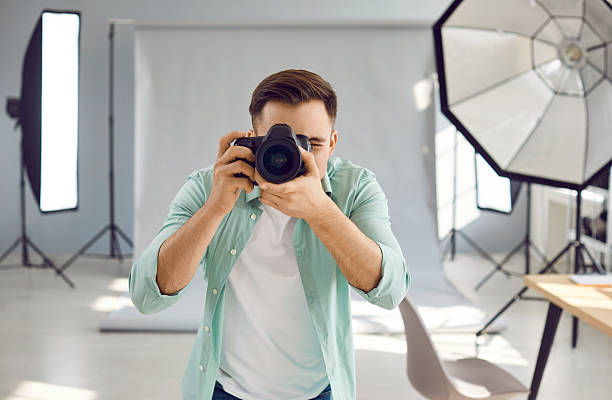 istock Professional photographer standing in studio, holding camera, and taking photograph 2253998500