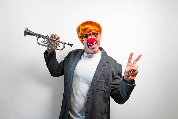 Man dressed as a clown holding a small trumpet and making a peace sign
