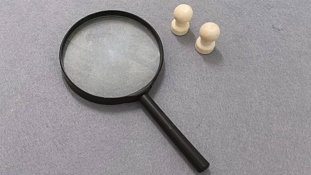 istock Magnifying glass and chess pieces on gray surface 2254011629