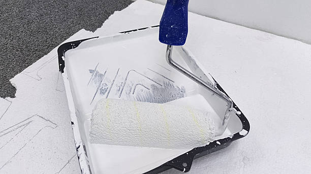 istock Painter's roller and tray with white paint on floor 2254011701