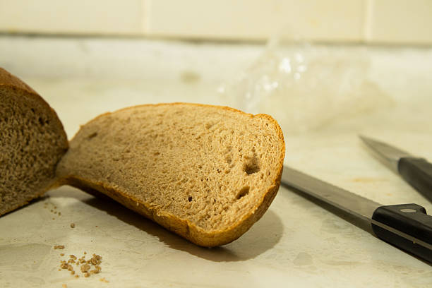 A person slicing fresh multigrain bread on a cutting board at a kitchen counter
