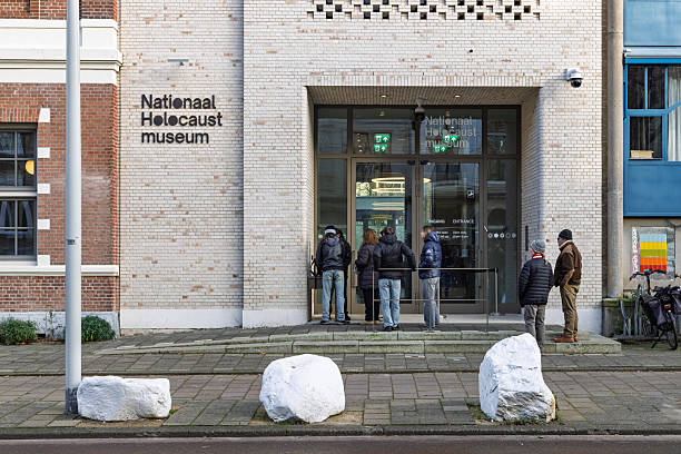 People waiting to enter the National Holocaust Museum in Amsterdam, featuring a white brick facade and glass entrance doors.