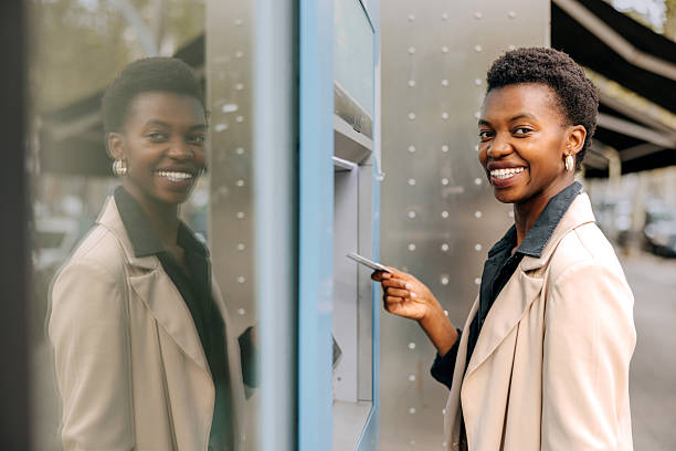 istock Well dressed smiling businesswoman posing for camera while using atm at city 2254028236